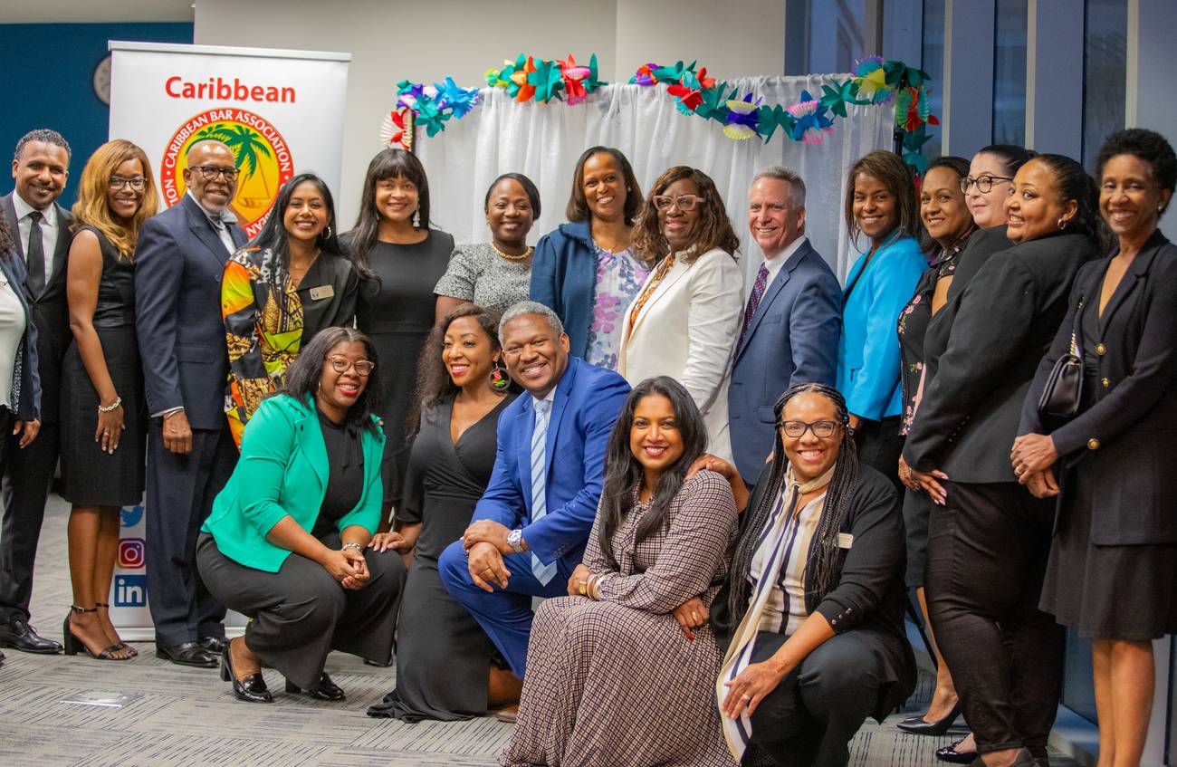 Members of the Caribbean Bar Association gathered together in front of the association banner and a flower-garlanded backdrop