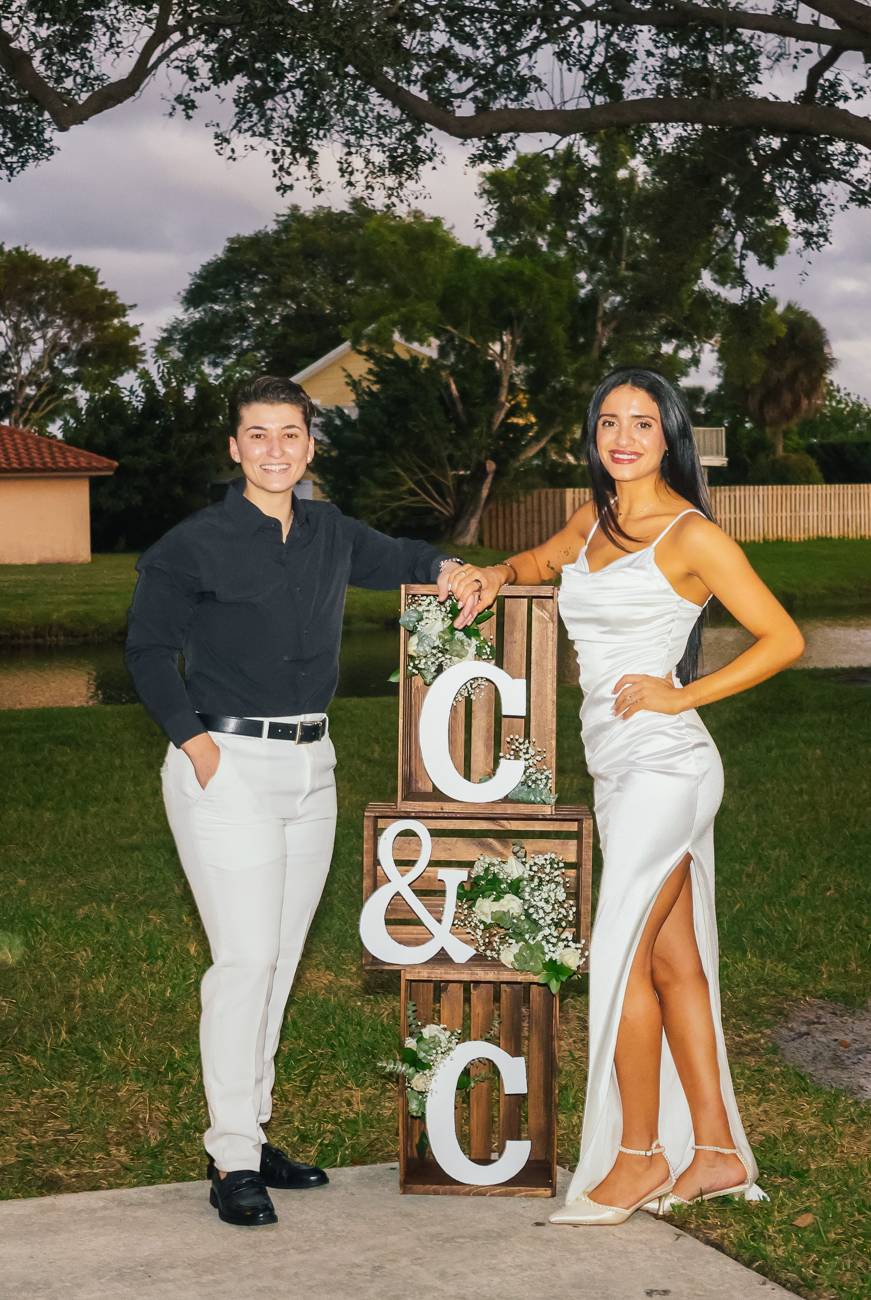 An engaged couple smiling beside wooden crates spelling C and C with white flowers