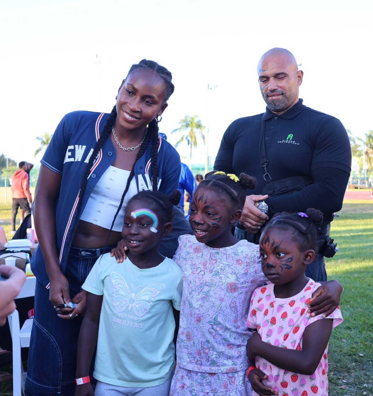 Coco Gauff smiling with three young girls with painted faces at her community celebration