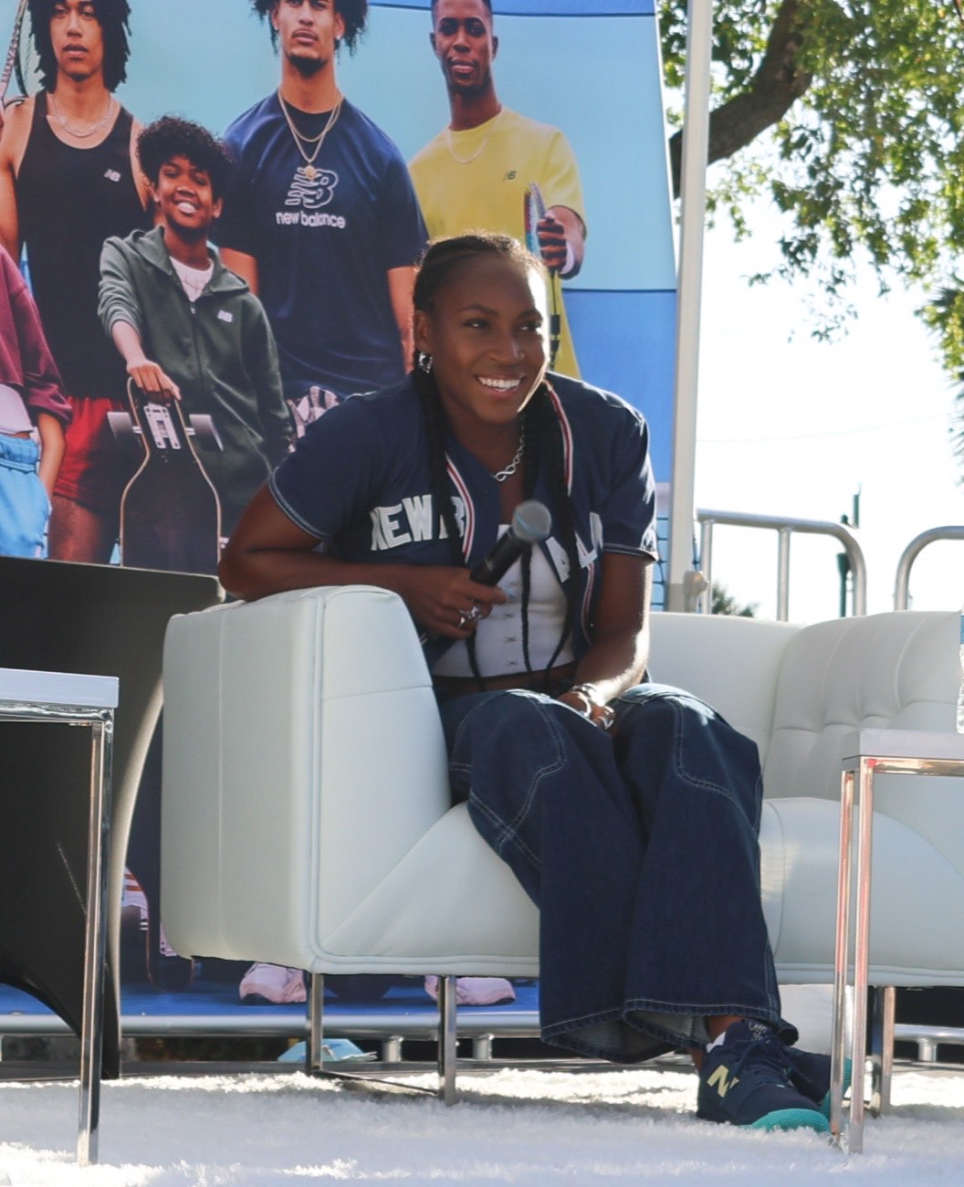 Coco Gauff smiling with a microphone in front of a New Balance backdrop at her Pompey Park community celebration