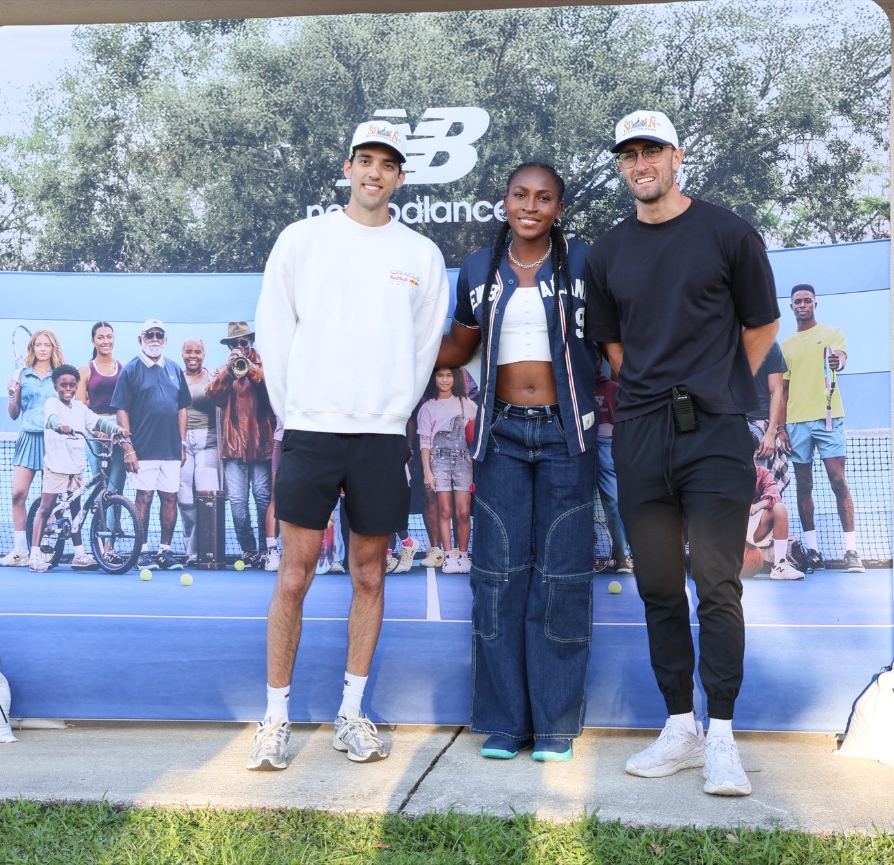 Coco Gauff standing with two members of the New Balance team in front of the photo backdrop