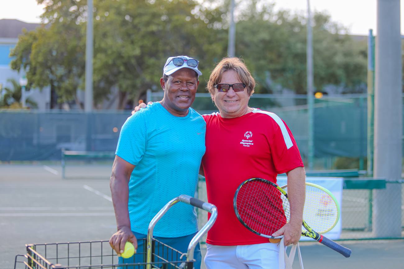 Two smiling coaches with rackets beside the ball cart at the tennis courts