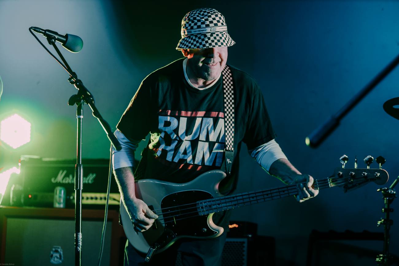 Goat Rope's bassist in a checkered bucket hat grooving under blue and green stage light