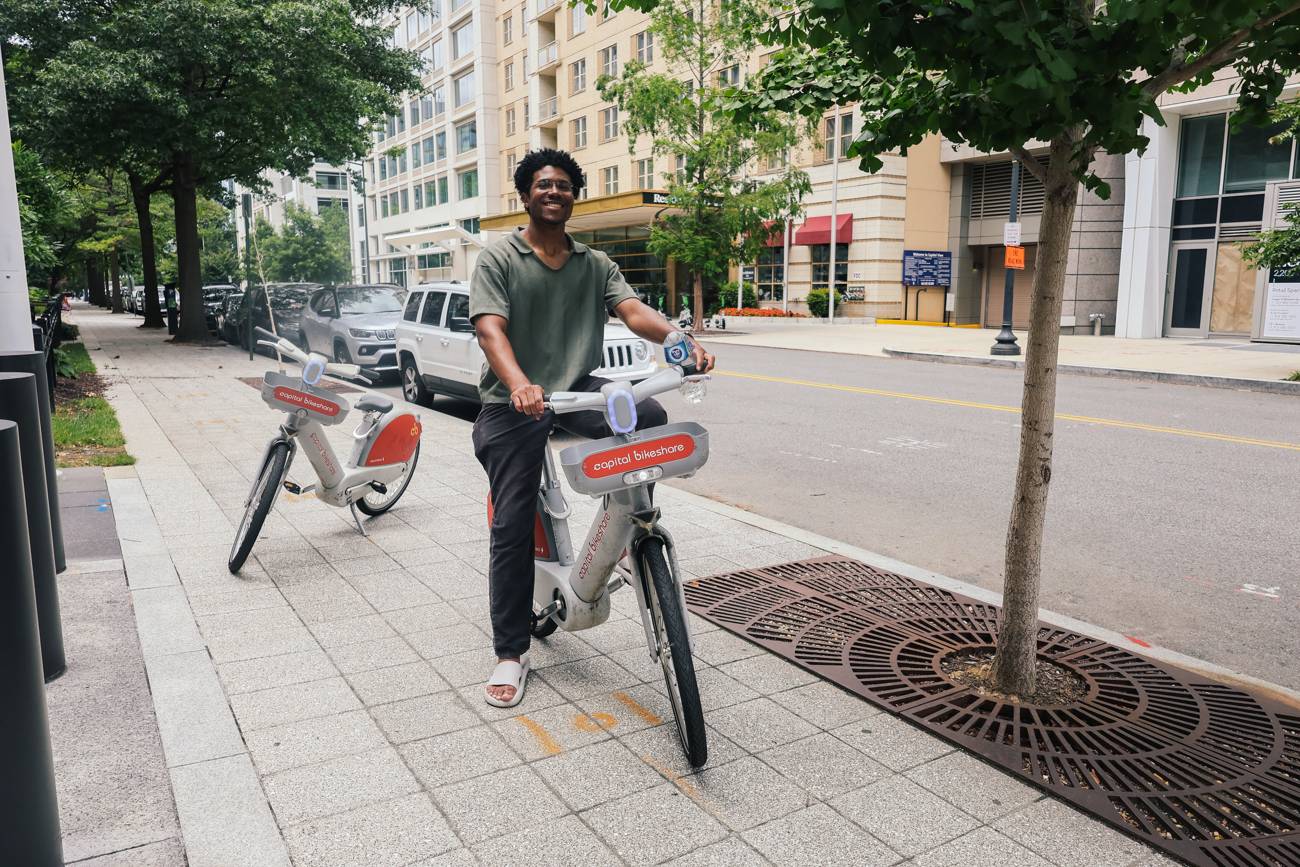 A young man pausing on a red bikeshare bicycle on a Washington street