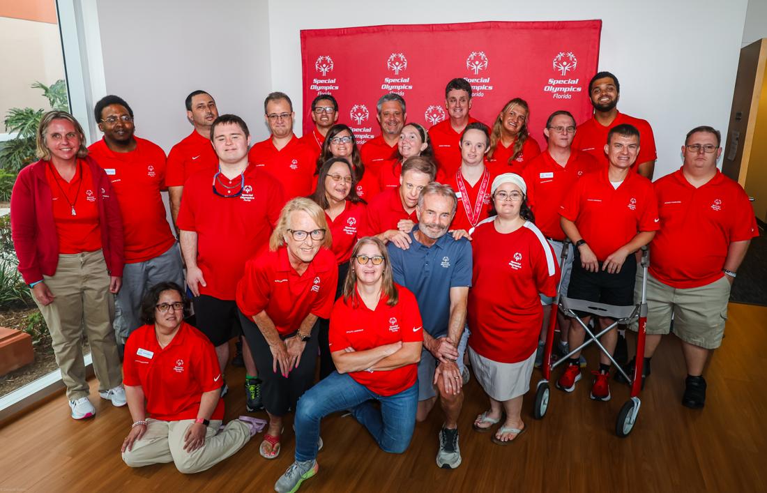Special Olympics Florida athletes and coaches gathered in red team shirts in front of the Special Olympics backdrop, all smiles