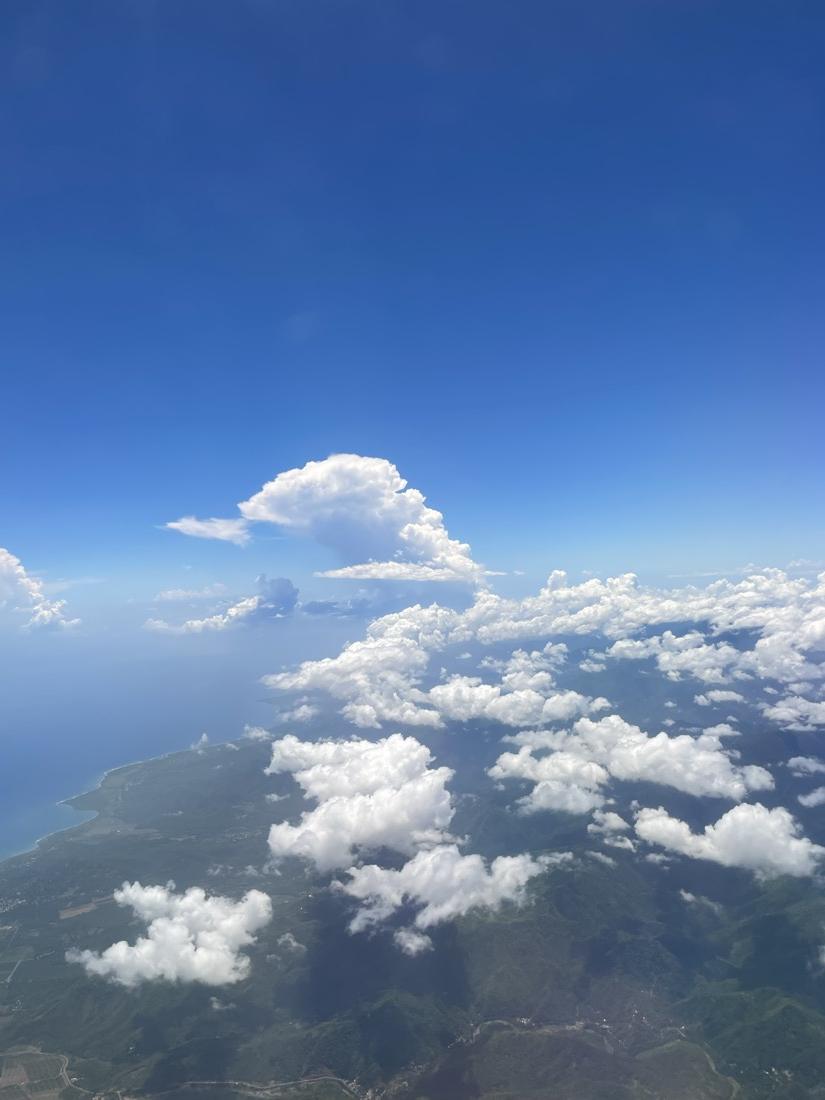 The view from an airplane window, mountains and clouds far below a deep blue sky