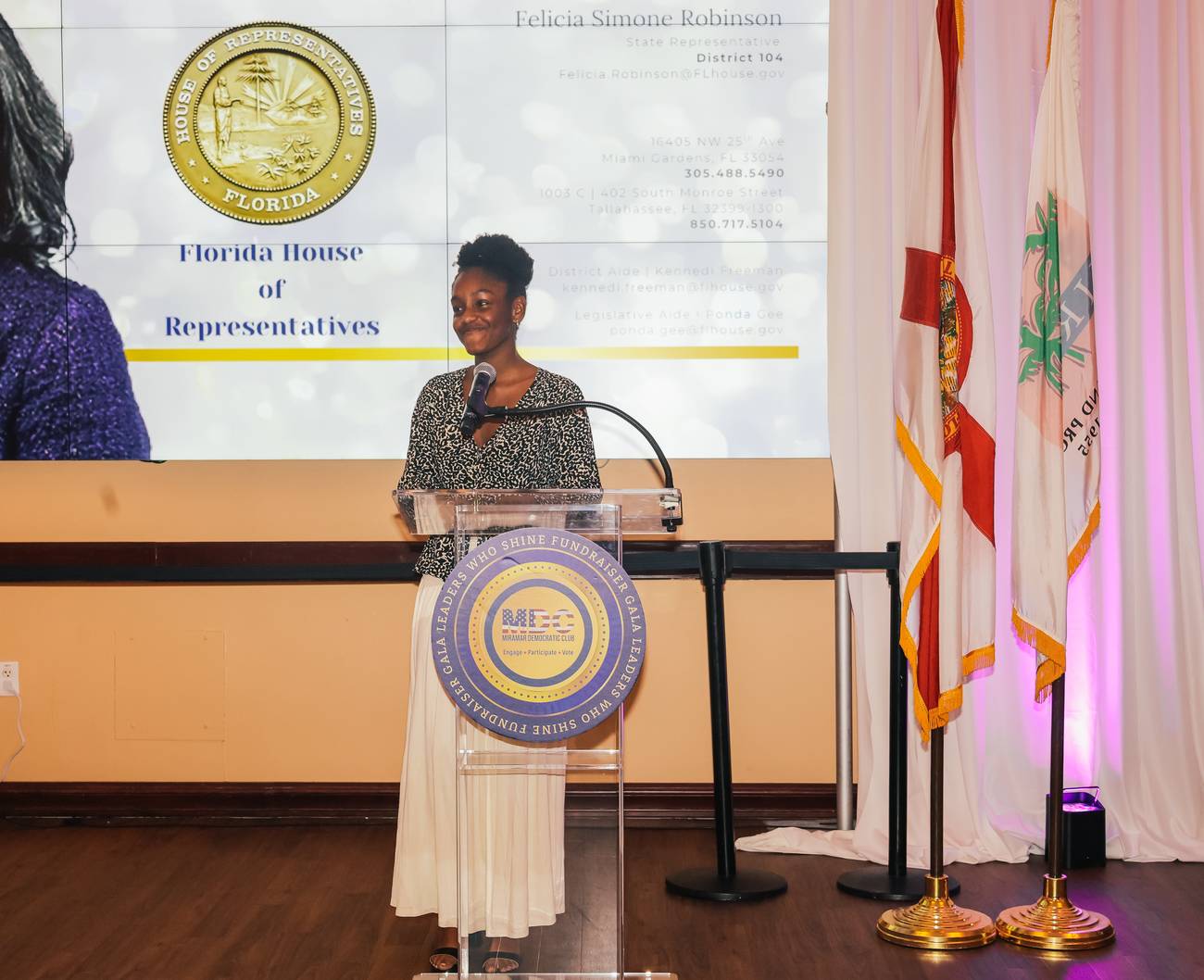 A speaker at the podium beneath the Florida House of Representatives slide for Rep. Felicia Simone Robinson at the Leaders Who Shine Gala