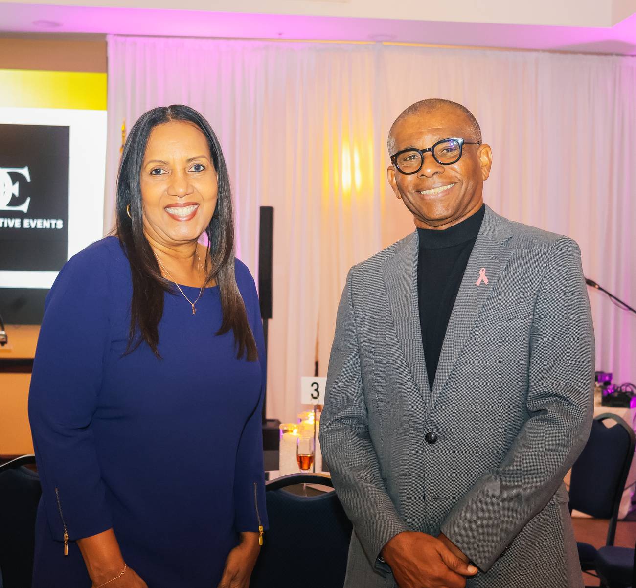Two guests in blue and gray, one wearing a pink awareness ribbon, smiling at the Leaders Who Shine Gala