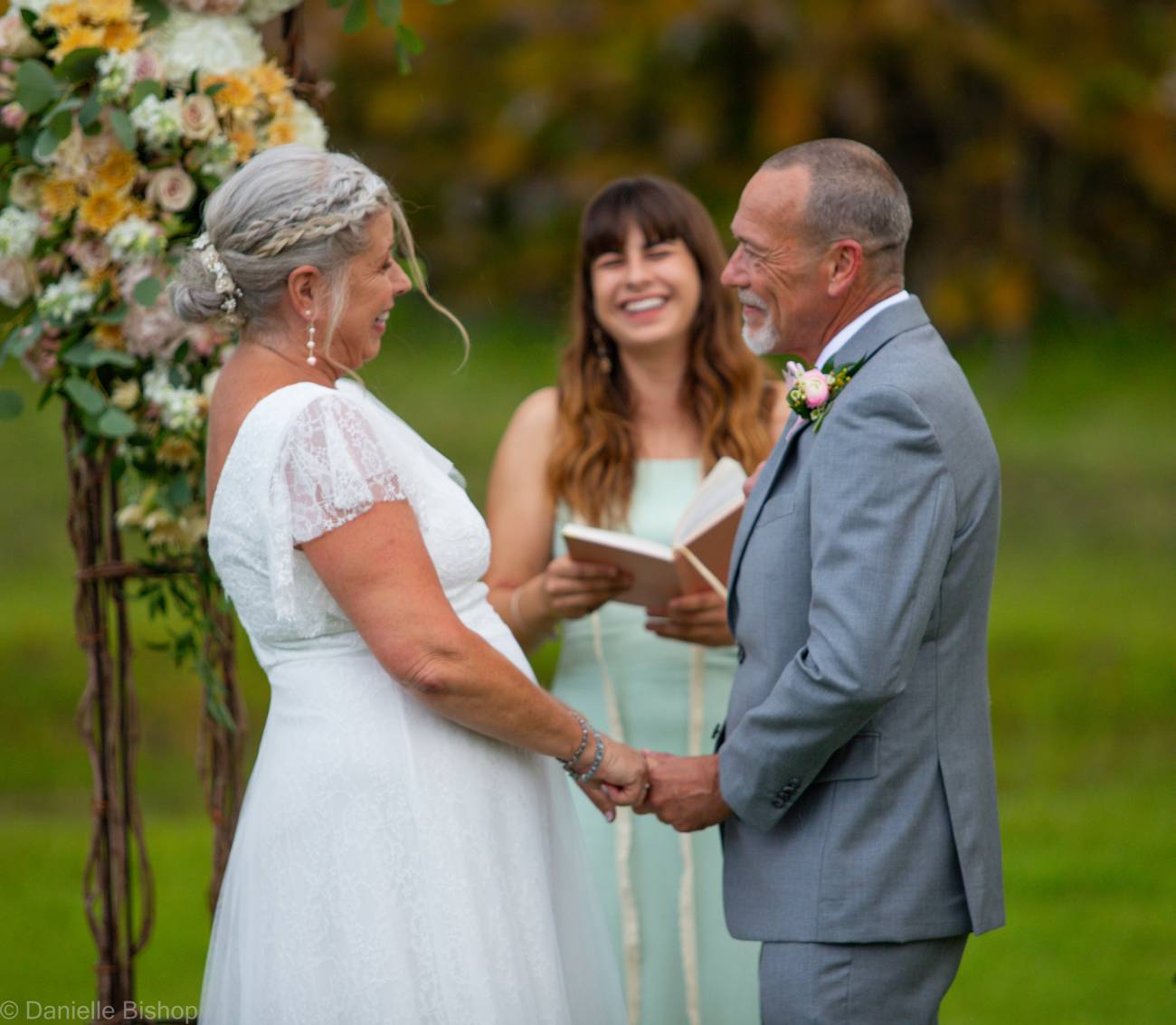 A bride and groom exchanging vows beneath a floral arch