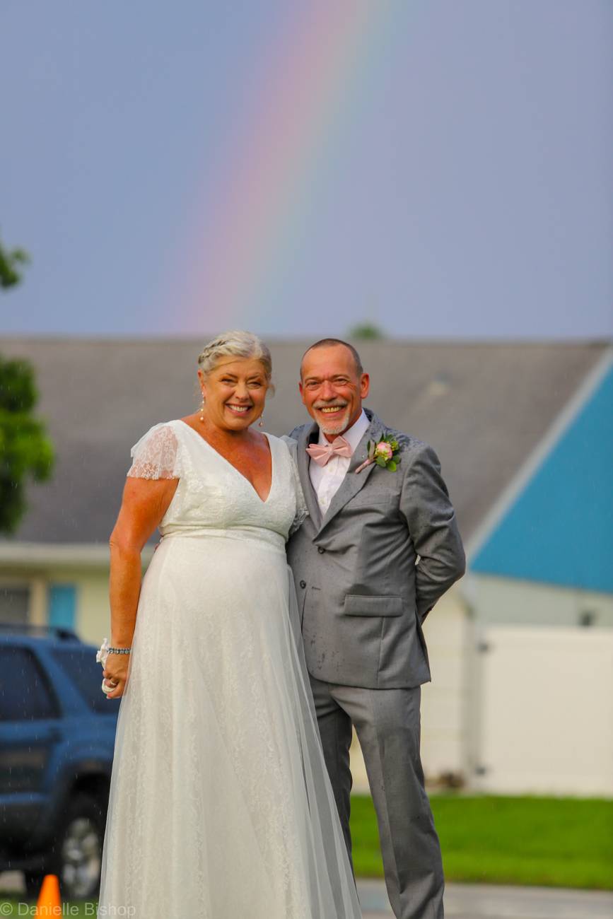 Newlyweds standing beneath a rainbow