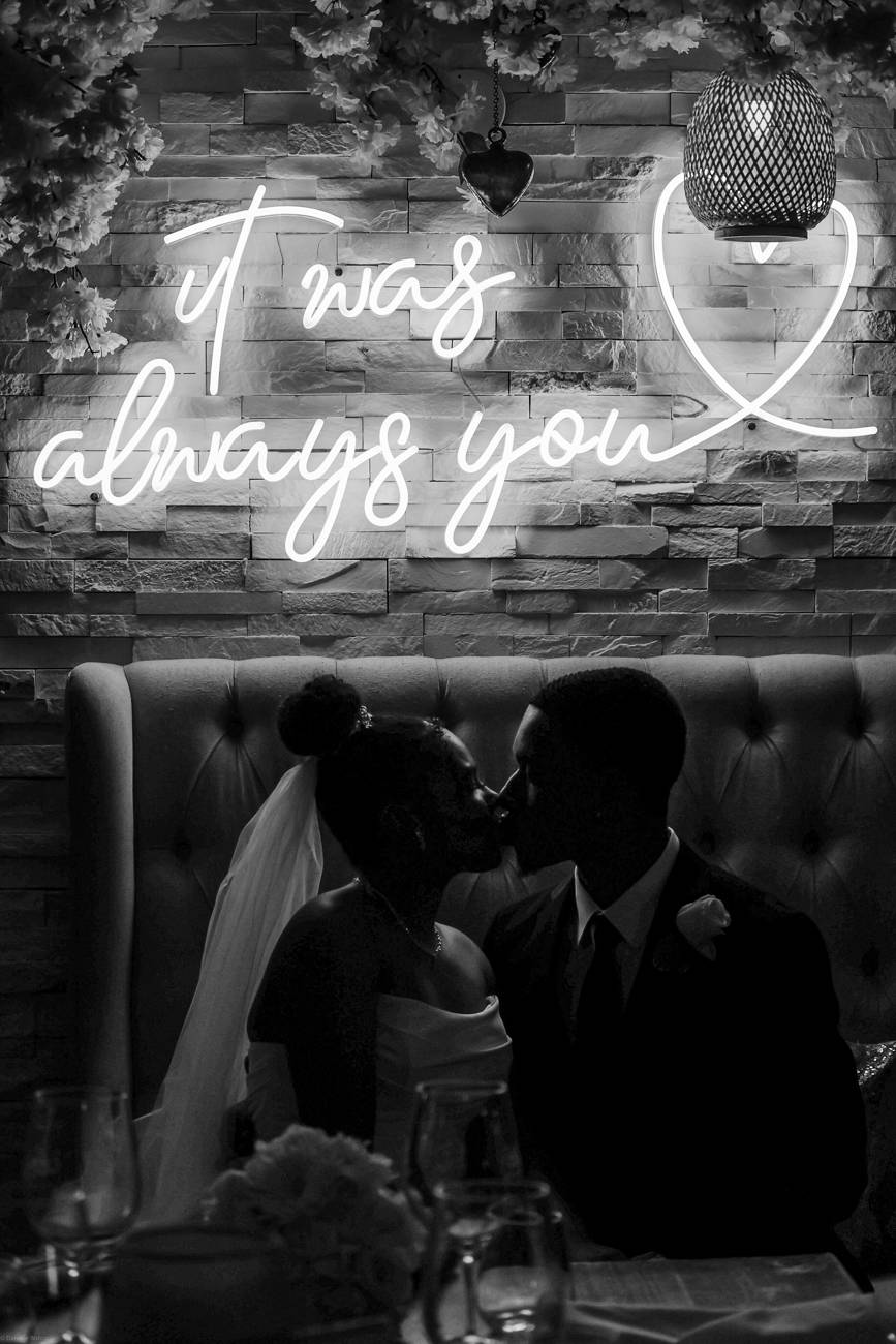 A silhouetted newlywed kiss beneath a neon sign reading it was always you