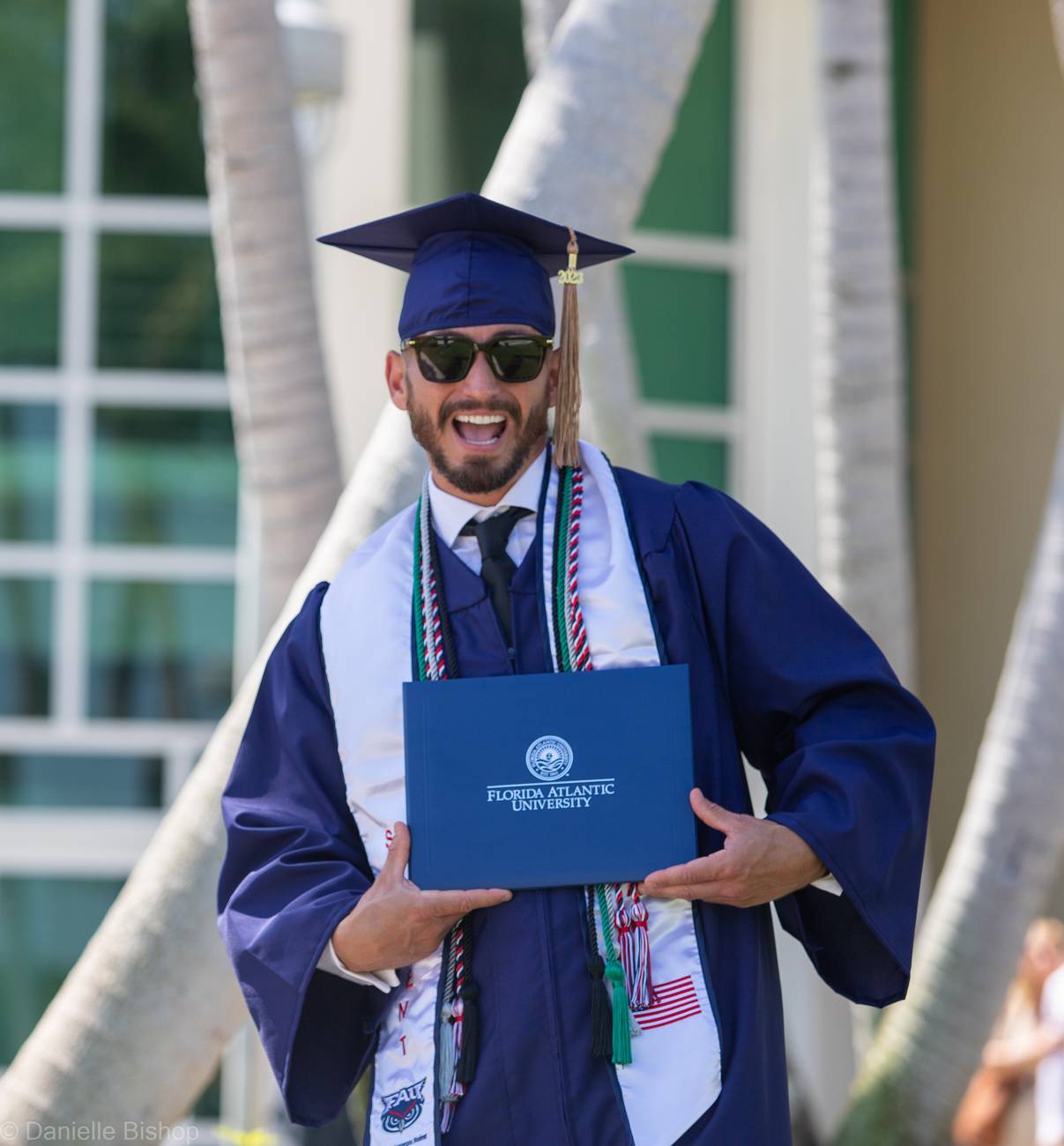 A graduate in cap and tie doing a flying kick off the pole above the FAU sign