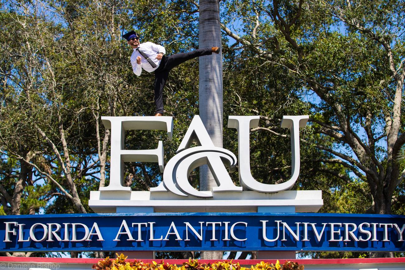 A joyful graduate in cap and gown holding his Florida Atlantic University diploma