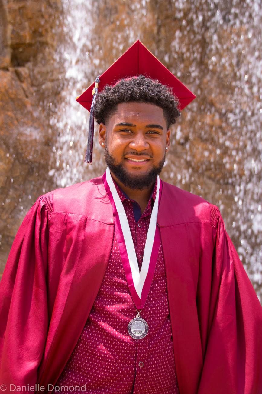 Graduate in maroon cap and gown by a waterfall