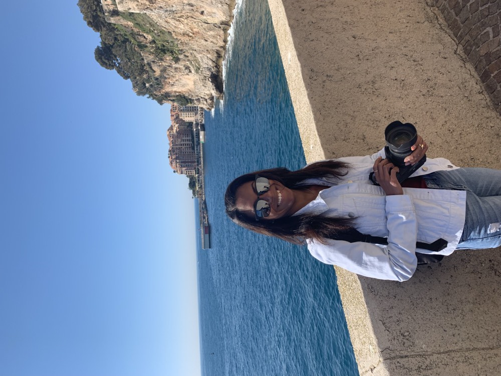 Danielle standing on the Mediterranean coast in Monaco with her camera, hair in the wind