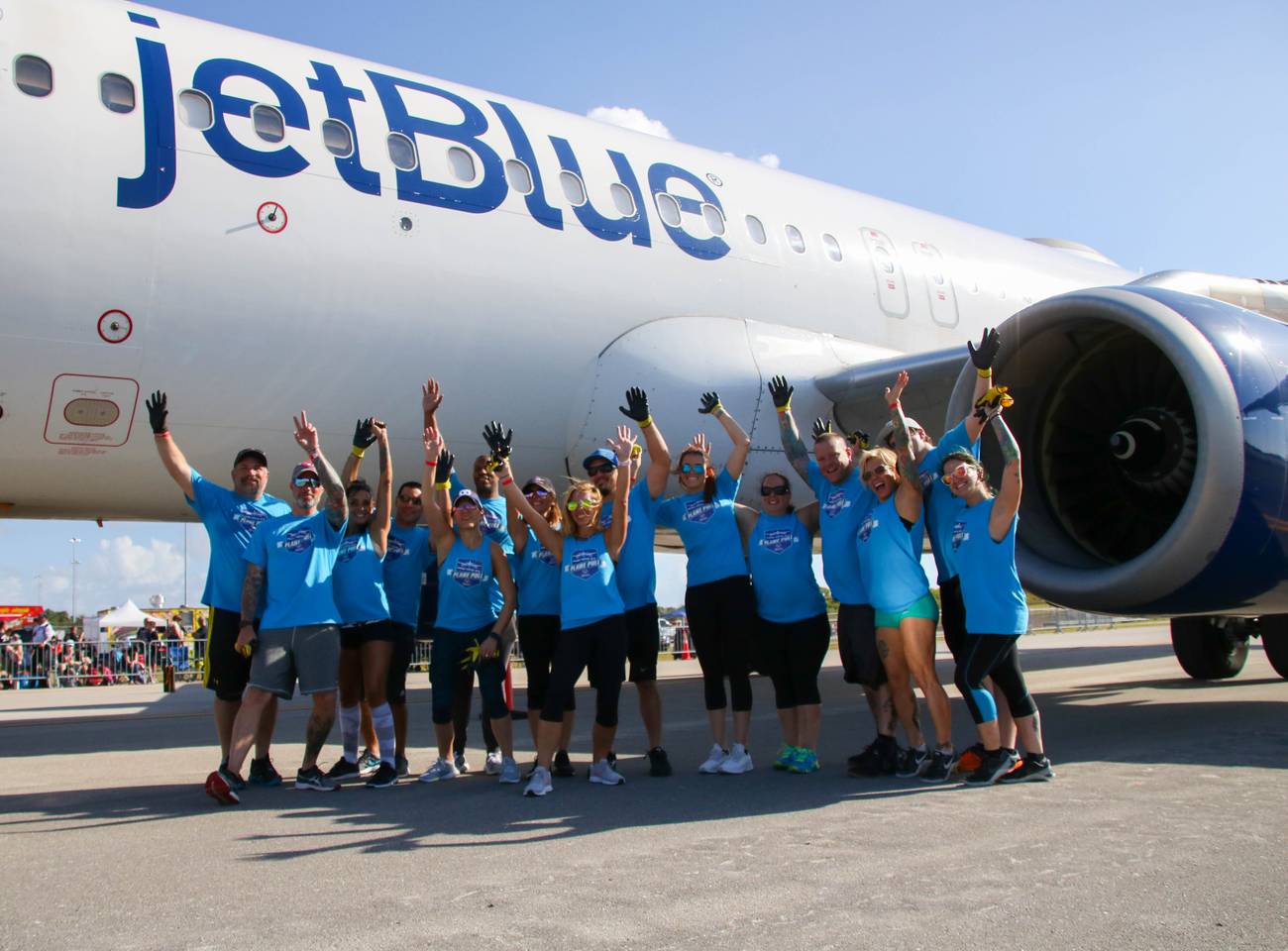 The Park Vista High School Plane Pull team cheering with raised arms beneath a jetBlue Airbus on the tarmac