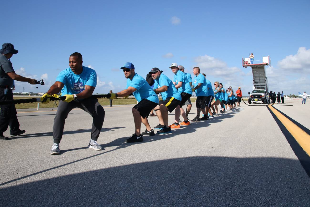 The Park Vista Plane Pull team leaning back on the rope in unison as they pull a jetBlue jet down the tarmac