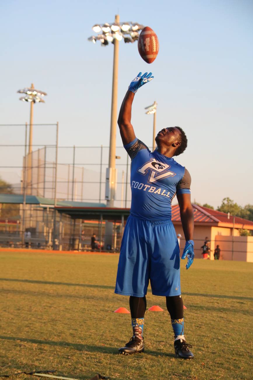 A Park Vista football player in blue reaching skyward for the ball under the practice field lights