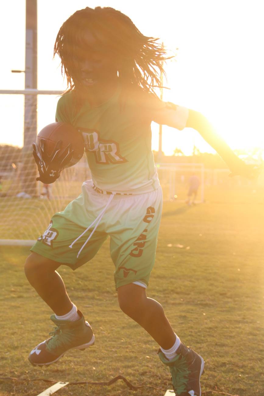 A young flag football player with flying hair sprinting through golden hour light, ball tucked tight