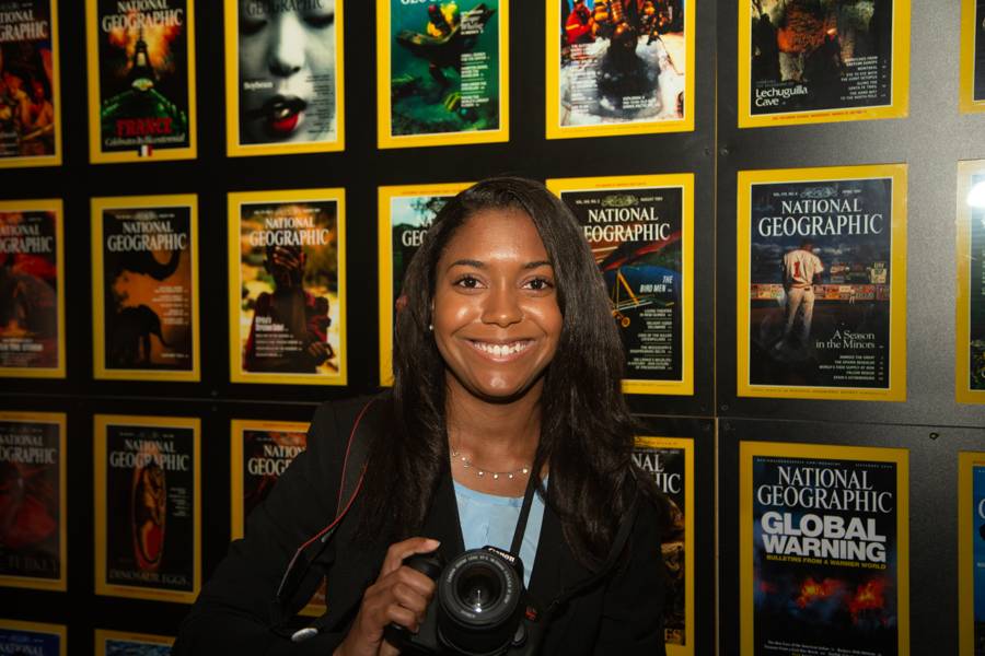 Danielle holding her camera in front of the wall of National Geographic covers at the magazine headquarters