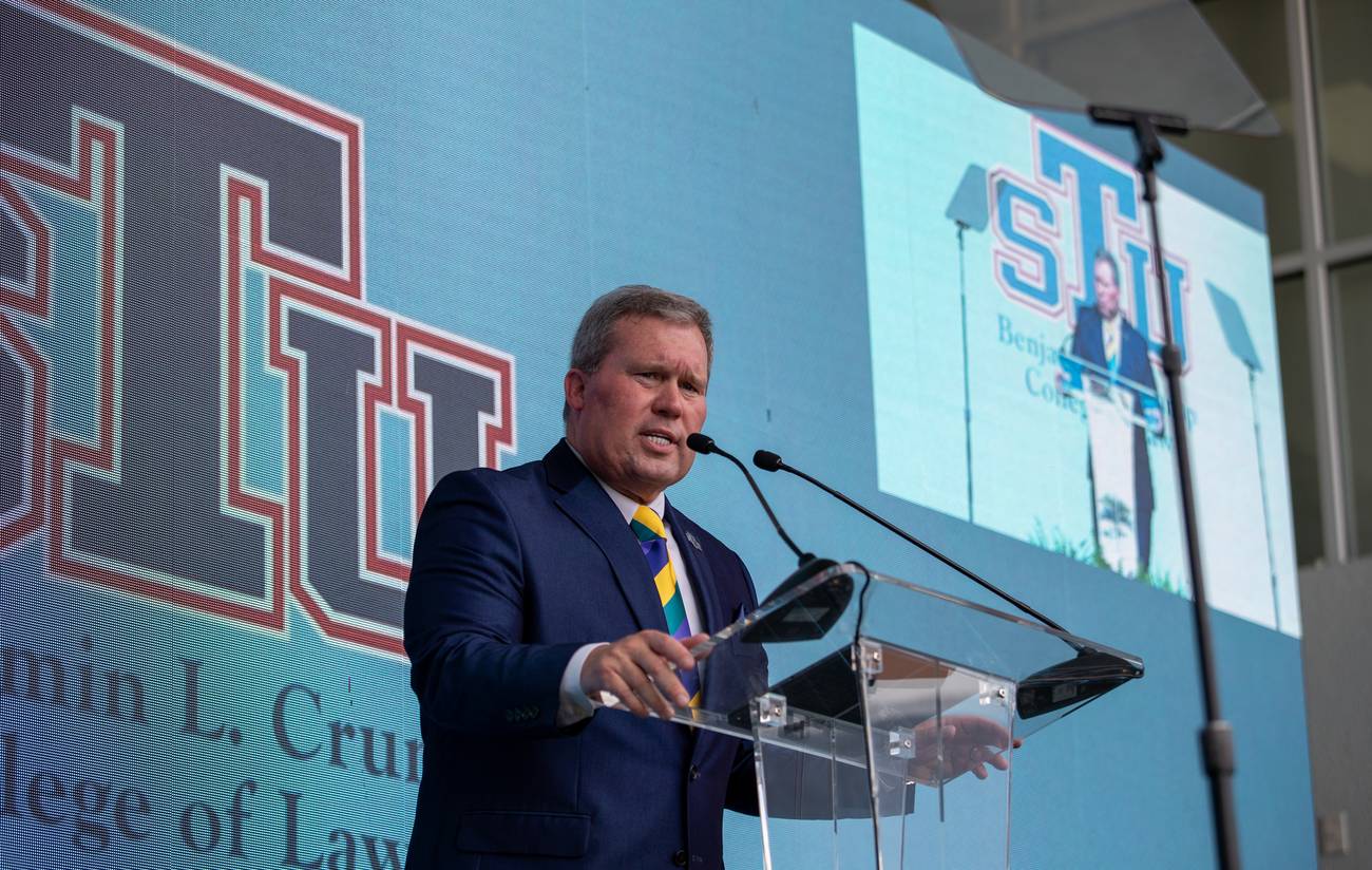 St. Thomas University President David A. Armstrong speaking at the podium in front of the STU logo