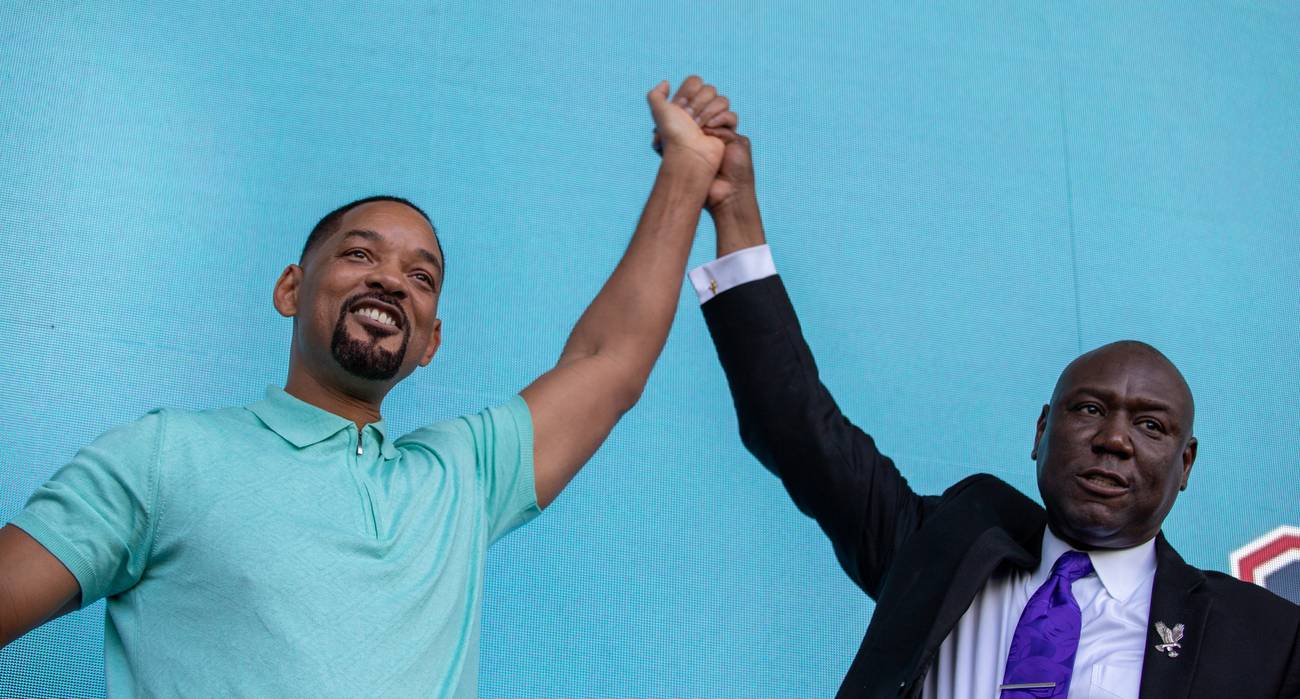 Will Smith and Ben Crump raising their joined hands in triumph on stage at the dedication