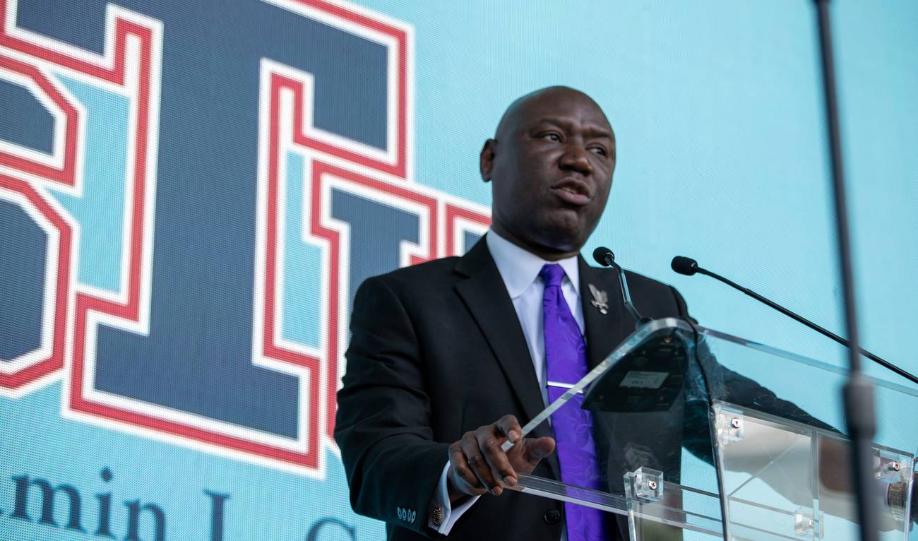 Attorney Ben Crump speaking at a clear podium in front of the St. Thomas University logo