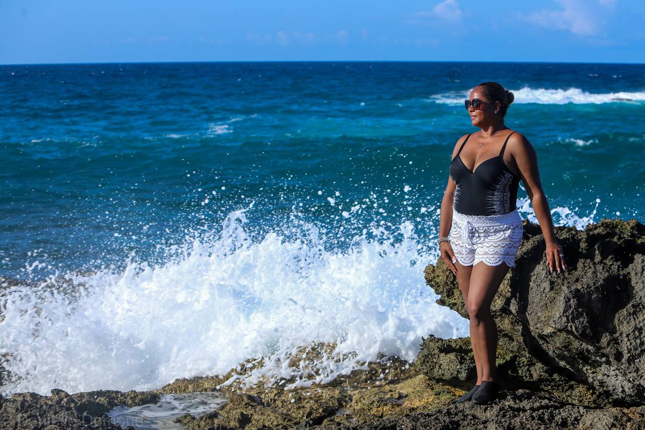 Woman standing on coastal rocks as surf crashes in Kingston, Jamaica