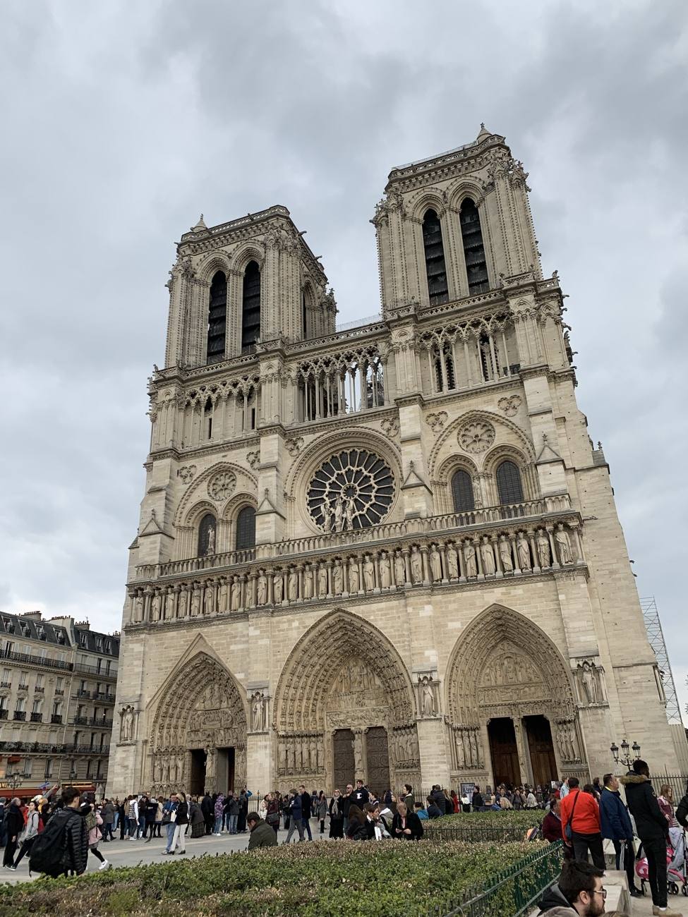 The facade of Notre-Dame cathedral in Paris under a gray sky, crowds gathered below