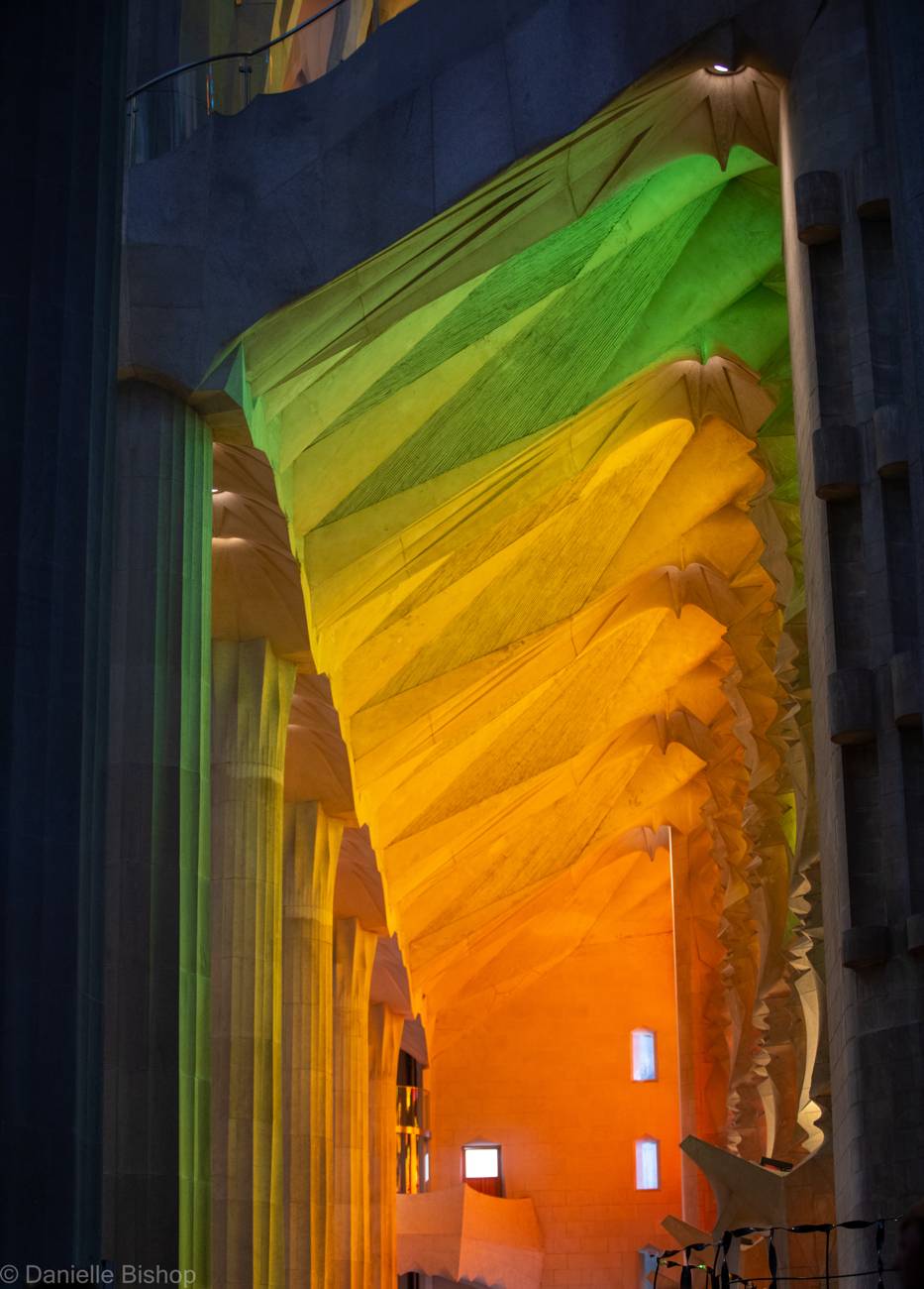 The vaulted stone ceiling of the Sagrada Familia glowing green, gold, and orange in the stained glass light